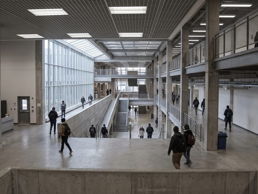 A university building atrium seen from above, students crossing an open floor and stairs.